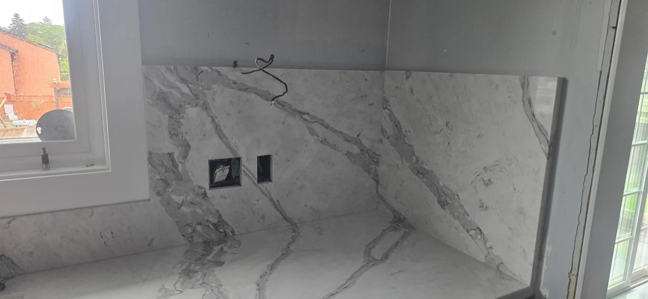 Grey veined quartz countertop with a matching full-height backsplash beside a window