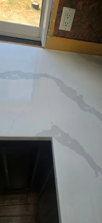 Grey veined quartz countertop corner and seam beside a window
