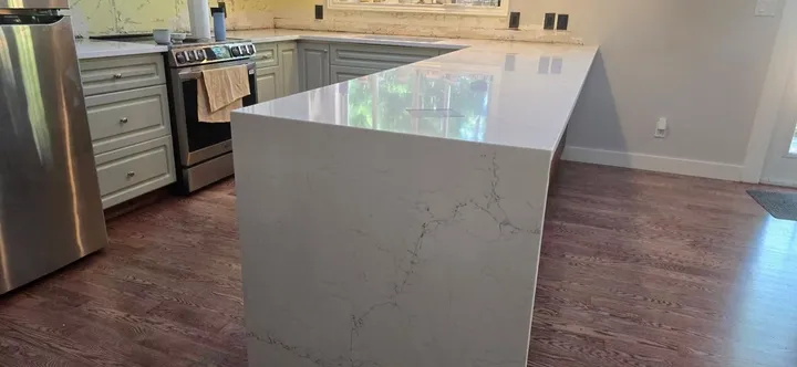 White quartz waterfall peninsula in a kitchen with grey cabinets